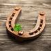 Rusted old horseshoe on a wooden table, with a four-leaf clover on top of it to symbolise good luck Thumbnail