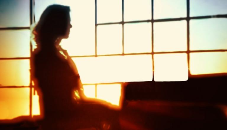 Woman in profile sitting in a chair at a desk, but the image is blurry obscuring her identity