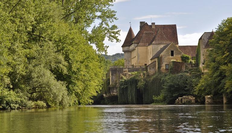 Castle on the right-hand side of a river bank with foliage on the left-hand side and a river in the middle