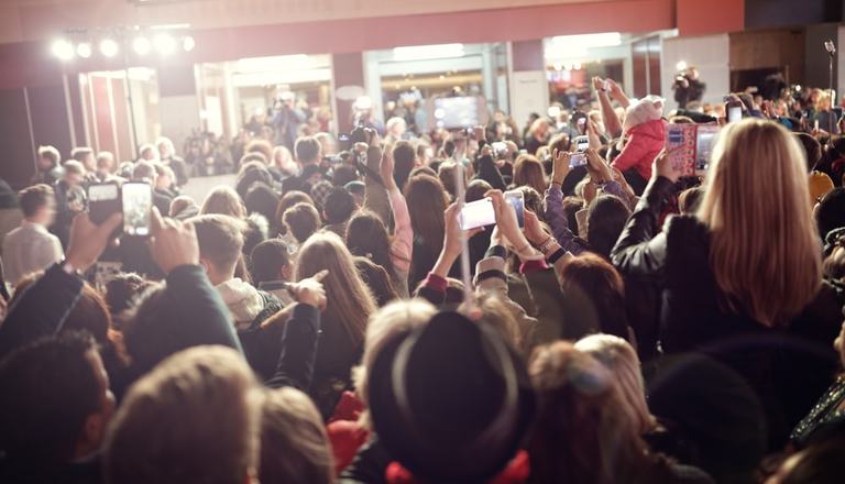 Behind shot of fans waiting for a celebrity to appear and taking photographs with their mobile phones