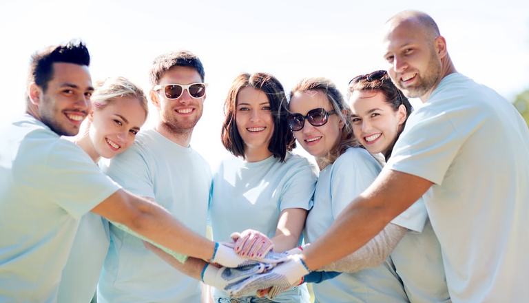 Group of adults smiling at the camera with hands together to suggest community and volunteering