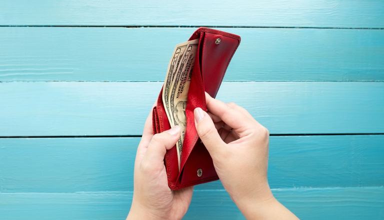 Woman's hands opening a wallet filled with dollar bills, background is wood painted blue