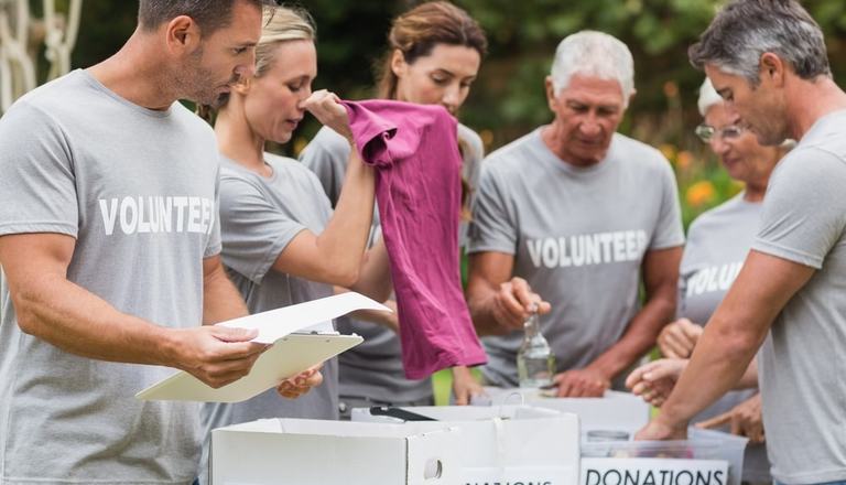 Group of people wearing Volunteer t-shirts, standing outside next to a table with donation boxes on it