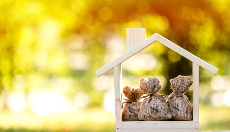 Small wooden house with bags of money inside to highlight investments