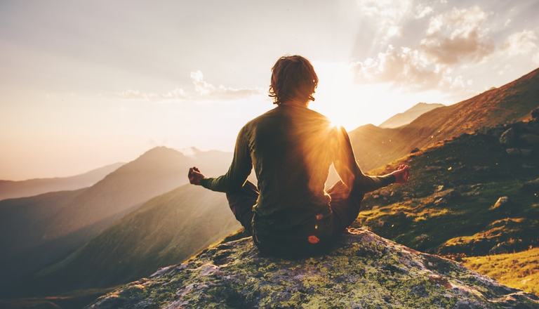 Calm man meditating with legs crossed as he looks over vast mountains