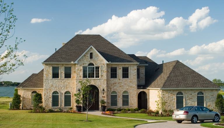 Large stone-and-brick mansion facing the camera, with a new silver car parked to the right