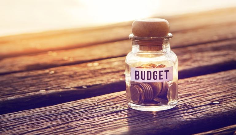 Glass jar on a wooden table, filled with coins and labelled "budget"