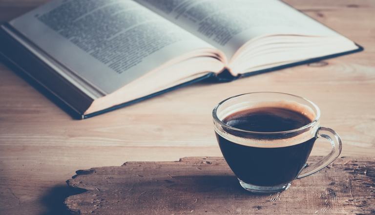 Dictionary laying open on a table, blurred text, accompanied by a coffee in a glass cup