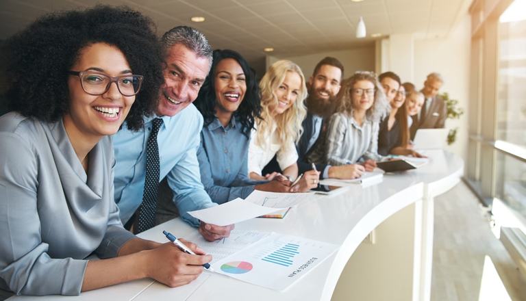 Lineup of multi-cultural employees leaning over a desk and smiling at the camera