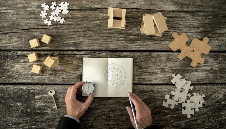 Puzzle pieces and a man holding a compass and notepad on a desk to signify different strategies