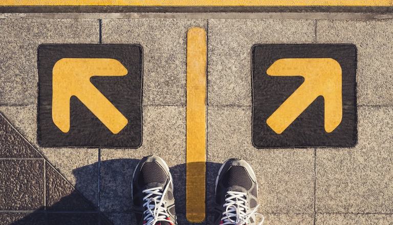 Man's feet standing between two arrows on the ground pointing in opposite directions