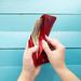 Woman's hands opening a wallet filled with dollar bills, background is wood painted blue Thumbnail