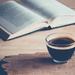 Dictionary laying open on a table, blurred text, accompanied by a coffee in a glass cup Thumbnail