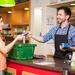 Male cashier at convenience store serving a female customer, customer paying with debit card Thumbnail