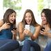 Three women sat on a couch holding cell phones, all are looking at the middle woman's phone and smiling and celebrating Thumbnail