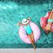 A bird's-eye view of two women lying in donut-style inflatable rings in a swimming pool Thumbnail