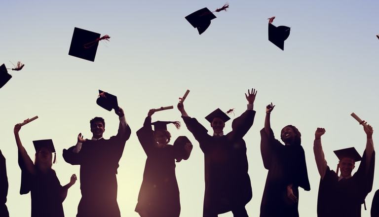 Silhouettes of a group of students throwing their mortarboards in the air to signify graduating